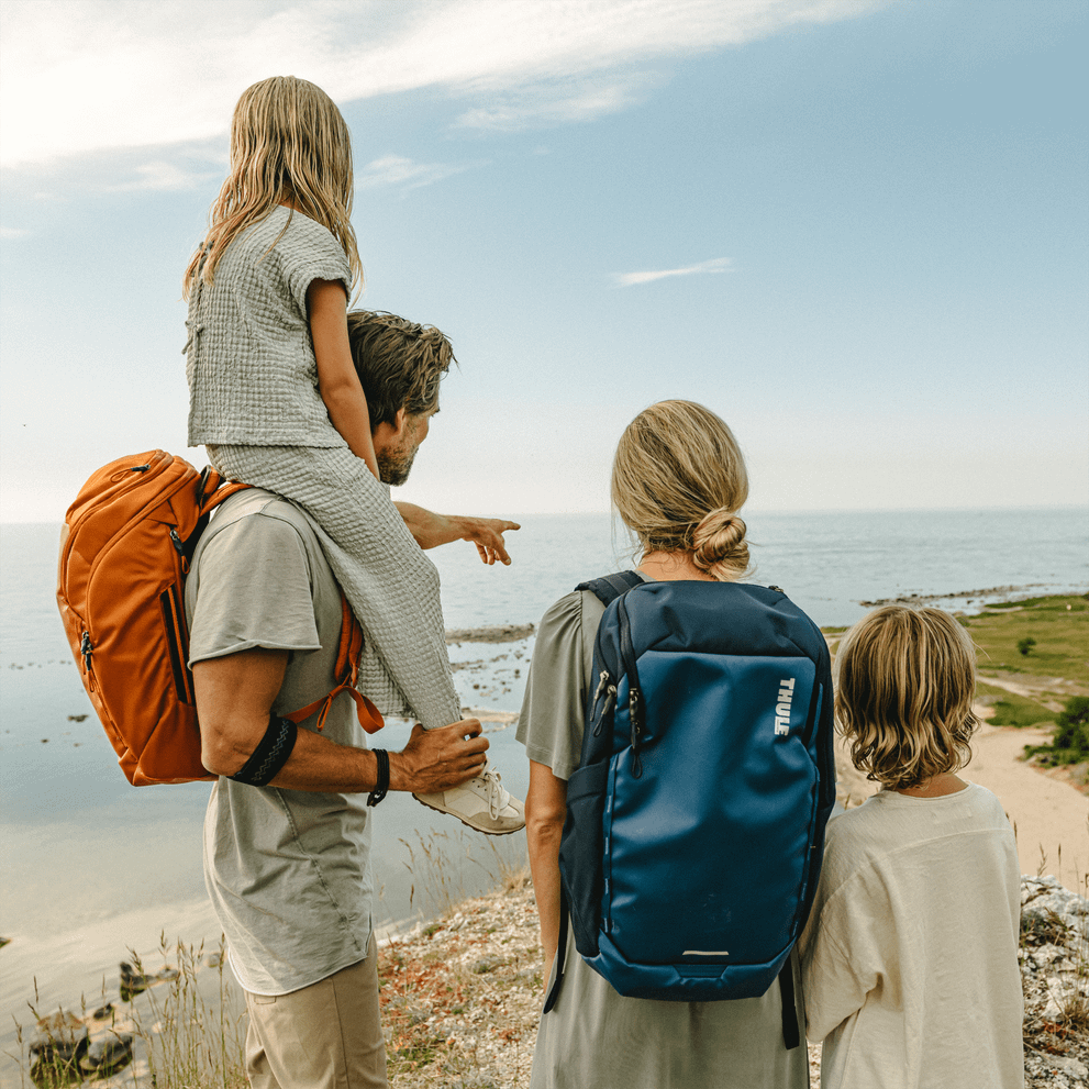 A family stands on a mountain looking at the ocean, holding Thule Chasm backpacks.