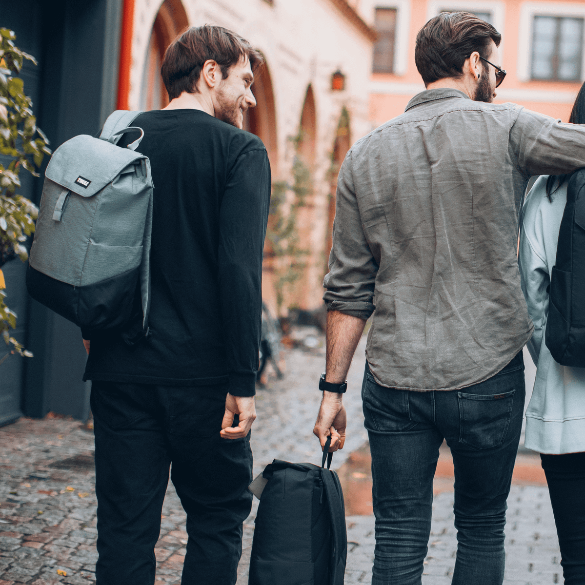 Four friends walk down a colorful, cobbled street carrying Thule Lithos backpacks.