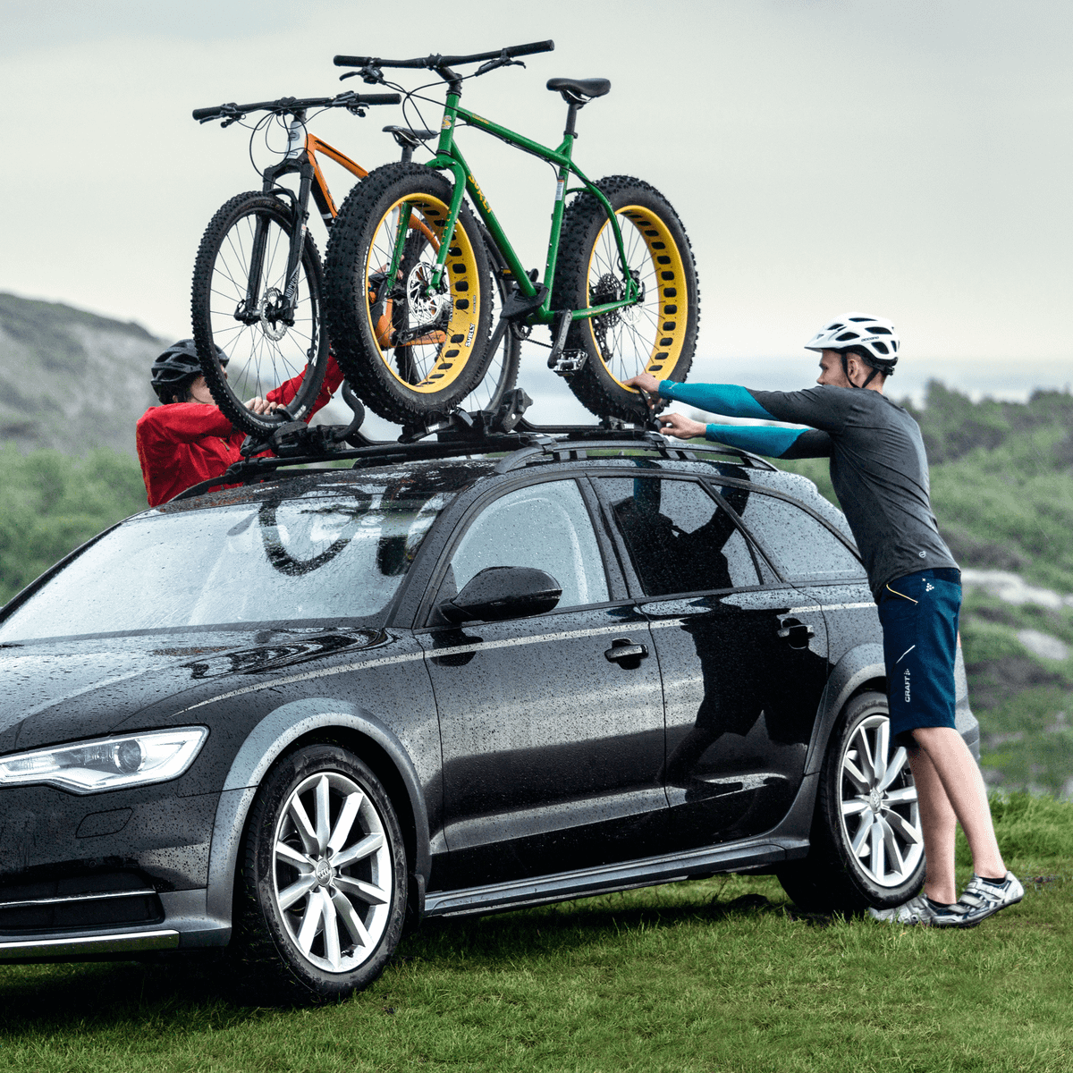 Two cyclists load their bikes onto a roof bike rack using the Thule ProRide Fatbike Adapter .