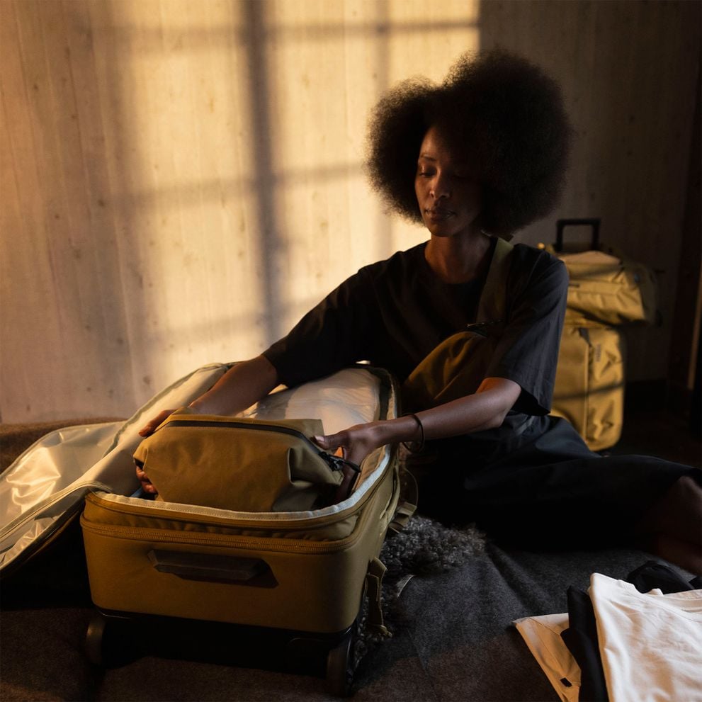 Woman placing a Thule Aion toiletry bag inside an open suitcase
