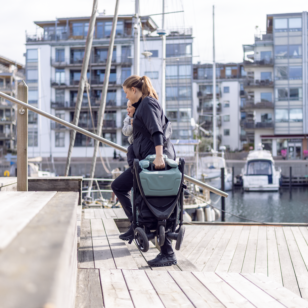 Woman carrying folded Thule Spring 2 stroller by the harbor.