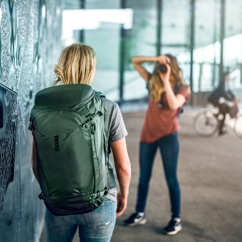 A woman is taking a picture of a friend with a Thule Landmark 40L travel backpack