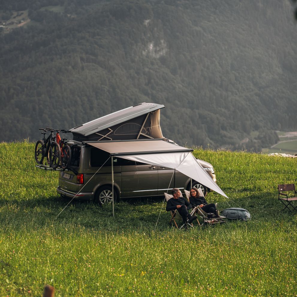 A lift-top van is parked in the mountains with a bike rack and Thule Subsola awning panels.
