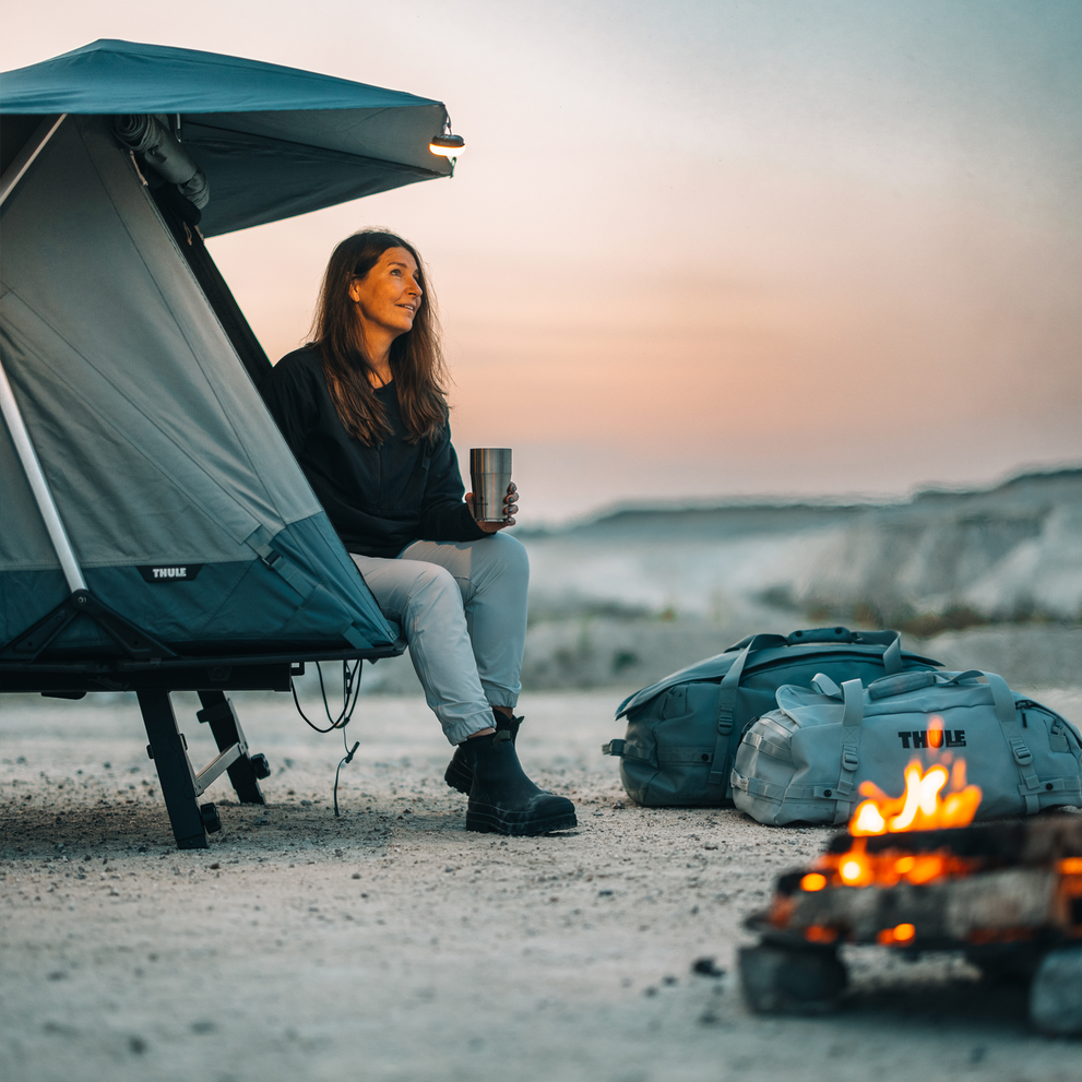 A woman is sitting inside a Thule Outset car tent enjoying an outdoors summer camping environment.