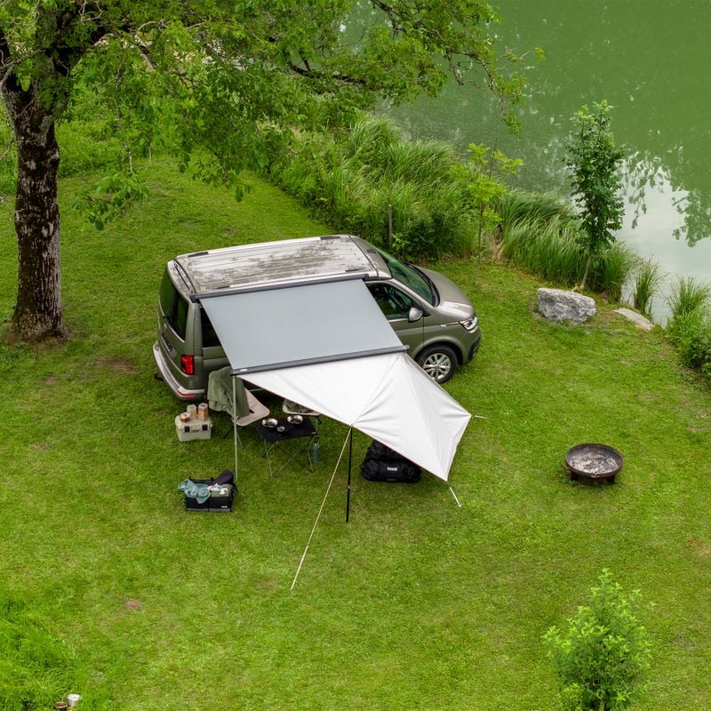 A van is parked next to the water with the Thule Subsola versatile awning panels.