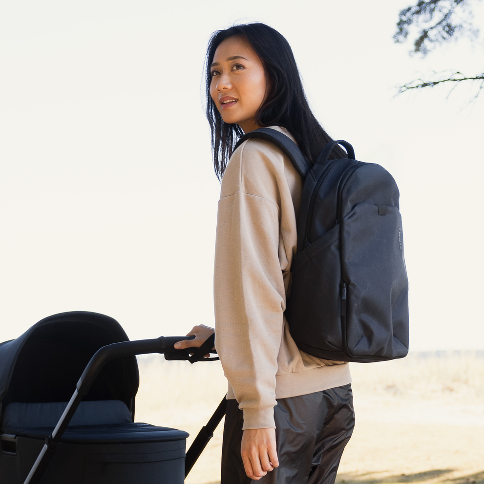 Adult wearing a Thule Aion changing backpack while standing next to a stroller.