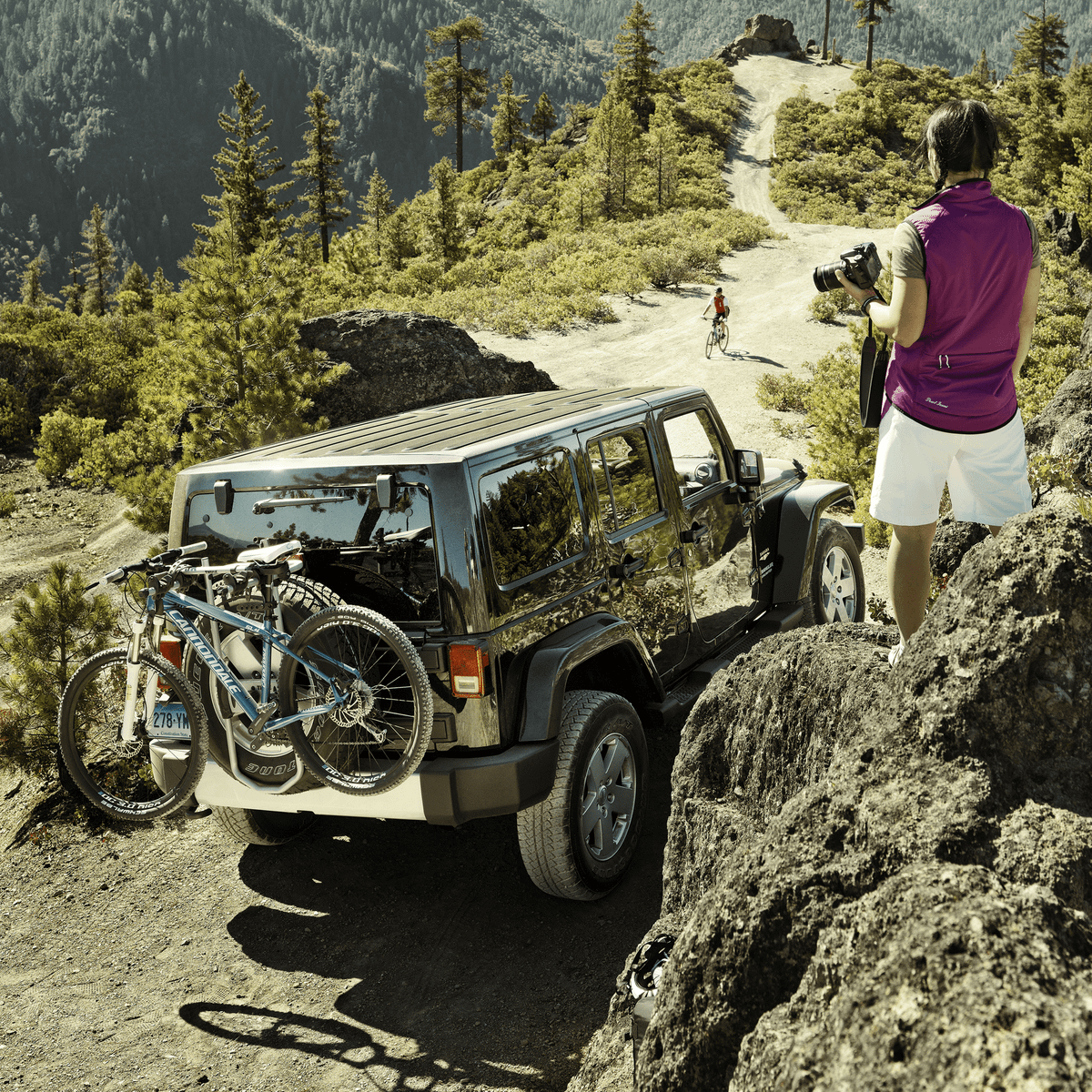 A person walks in the mountains next to a jeep with a Thule SpareMe Pro.