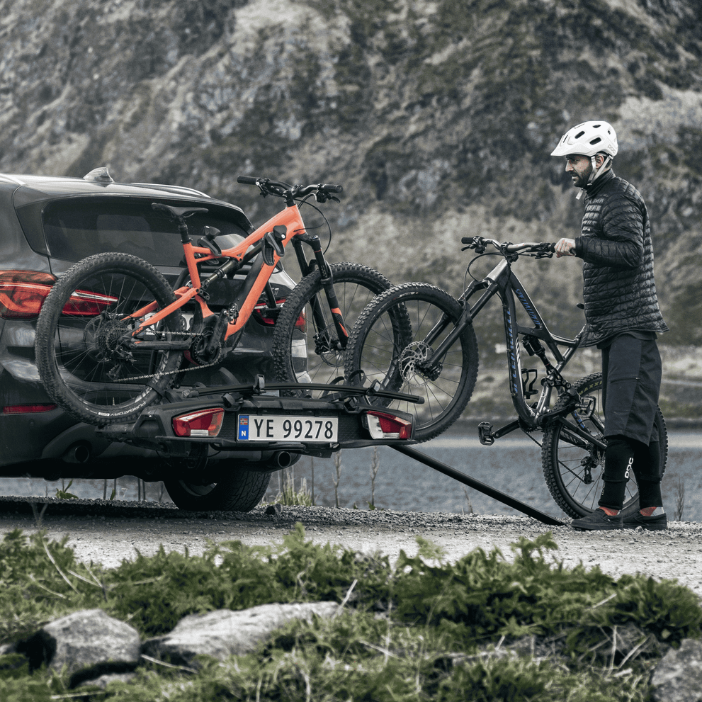 A cyclist loads their bike into a towbar bike rack with a Thule Loading Ramp XT