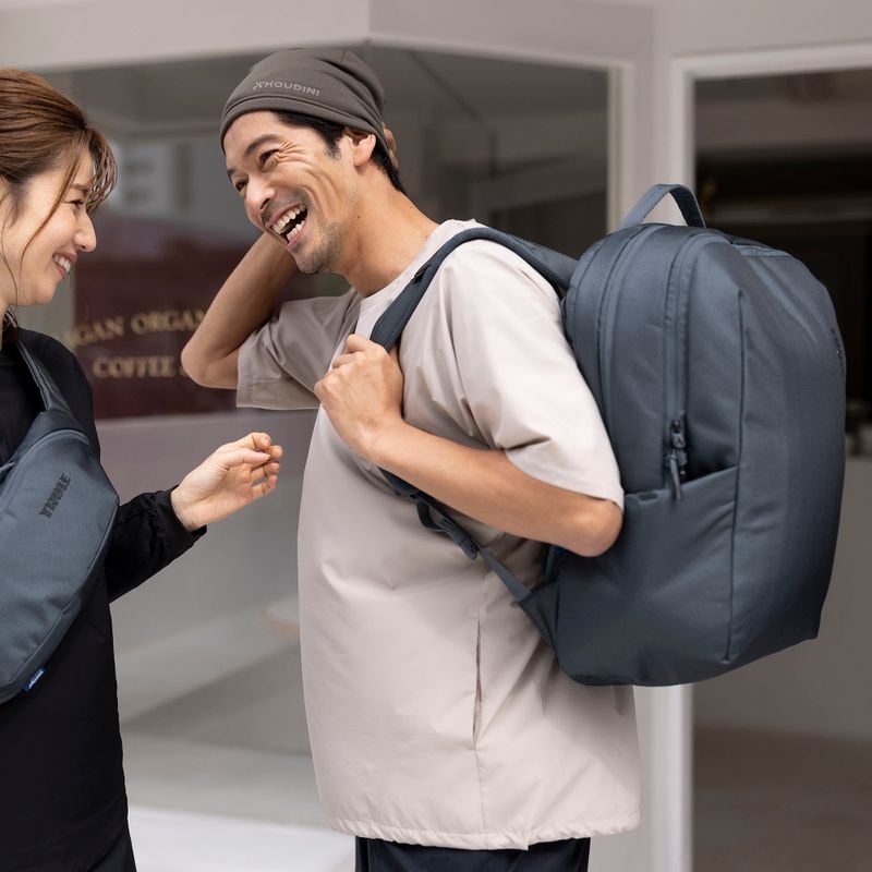 A woman and man laugh, one carrying a blue Thule Subterra backpack, the other a blue Thule Subterra sling.
