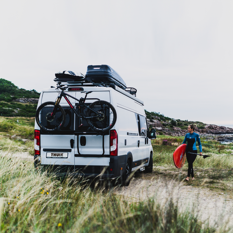 A white van parked in the grass with a Thule Elite Van XT Black van bike rack.