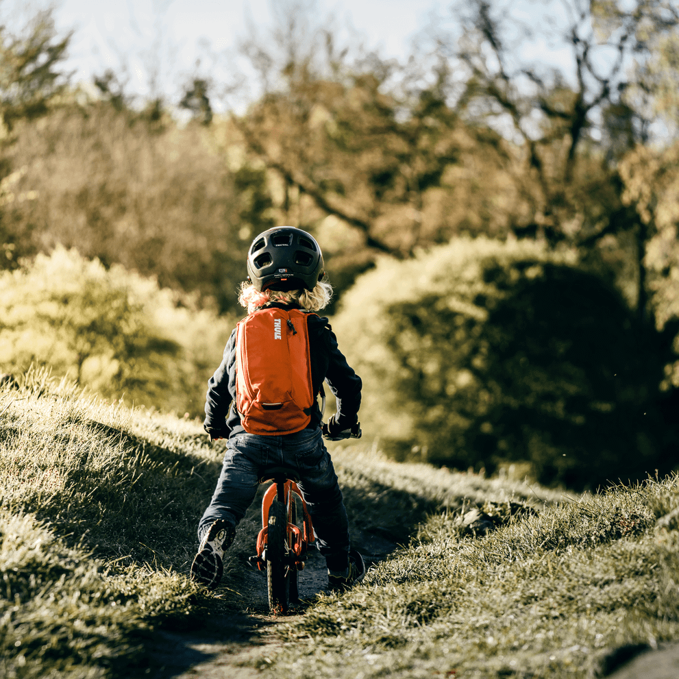A child goes mountain biking down a path with a Thule UpTake hydration pack.