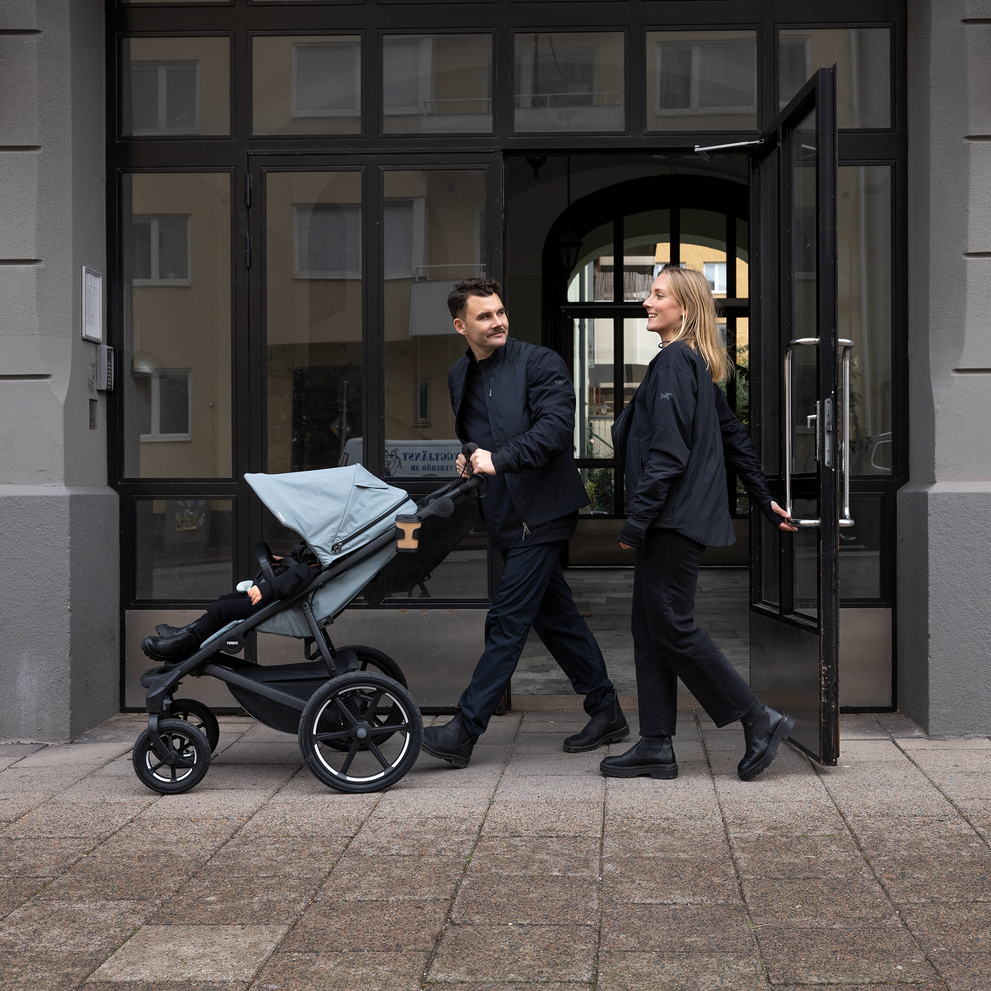 A man and a woman pushing the Thule Urban Glide 4-wheel stroller in front of a building.