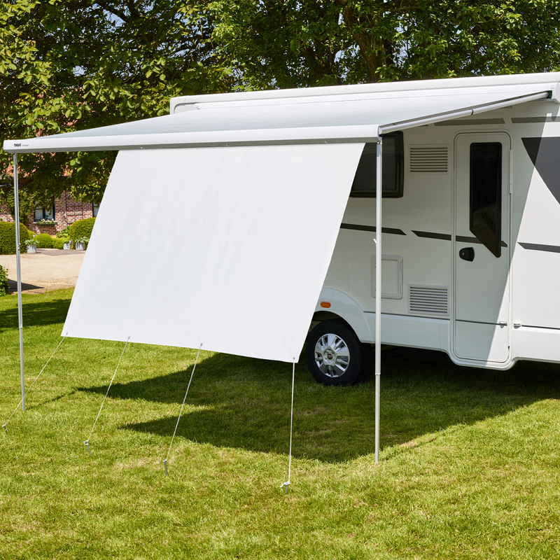 A white van is parked in the grass with a Thule View Blocker Side awning side wall.