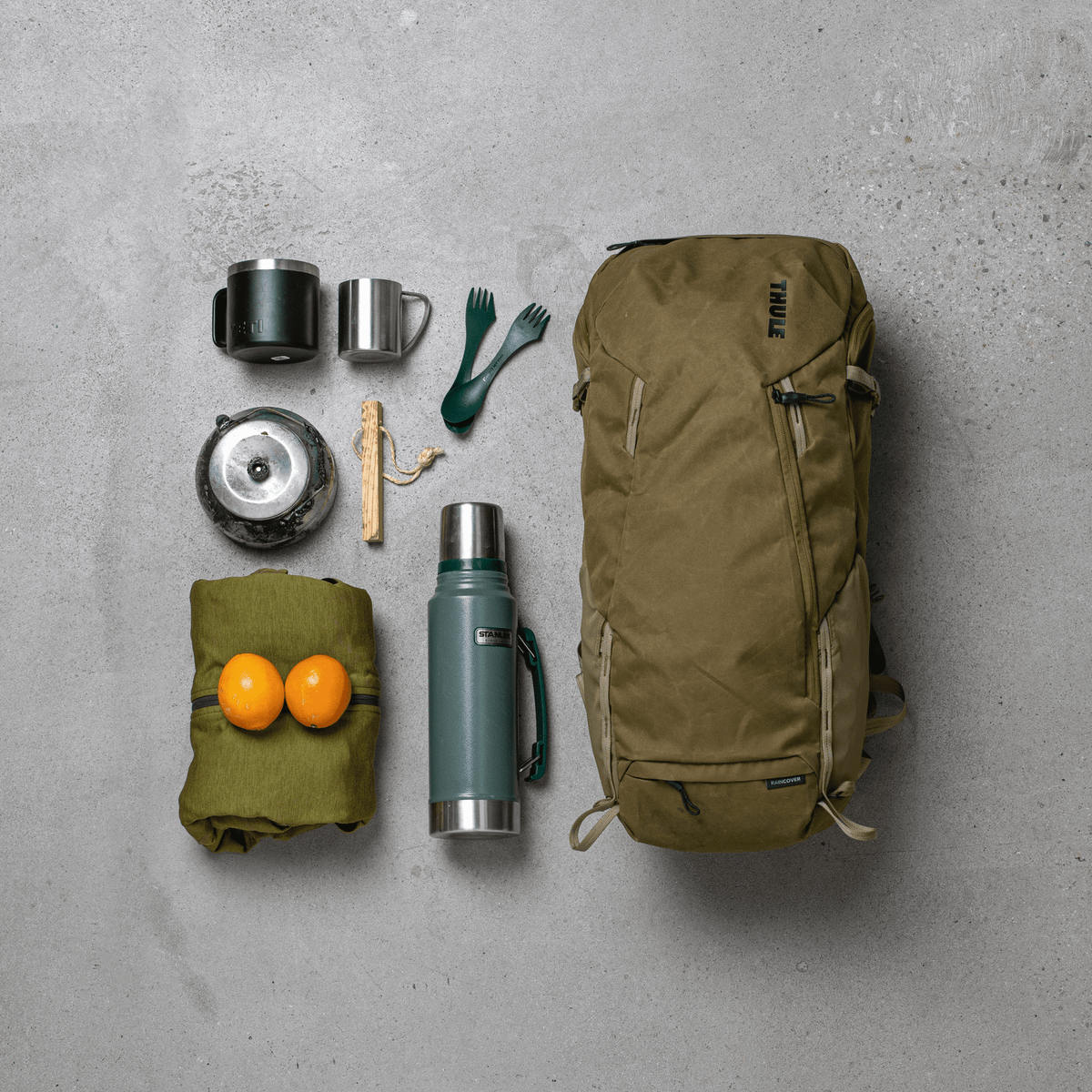 A Thule AllTrail X 35L hiking backpack lies on a concrete floor with hiking items placed around it.