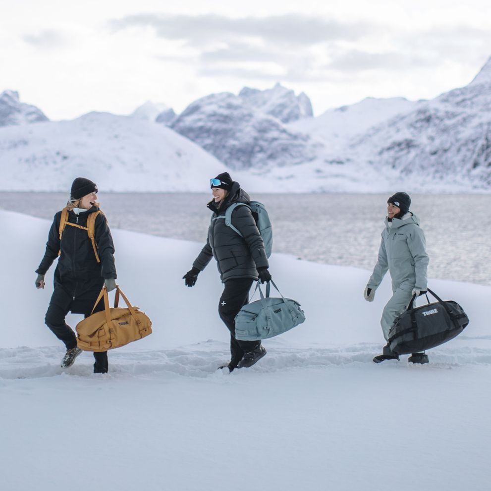 Three people walk through  snowy landscape with Thule Chasm duffels.