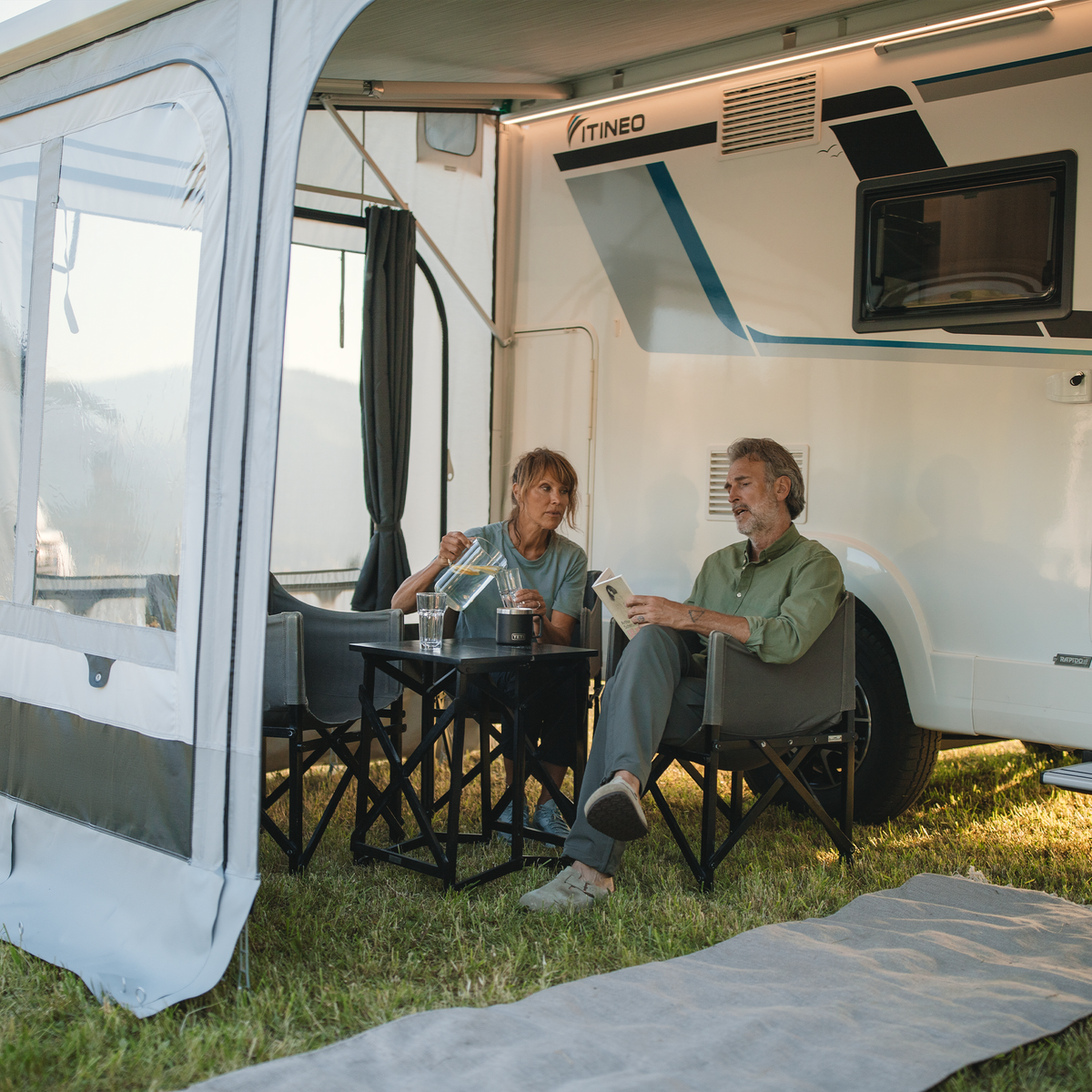 Two people sit next to a motorhome with a Thule Curtains rv awning curtains.