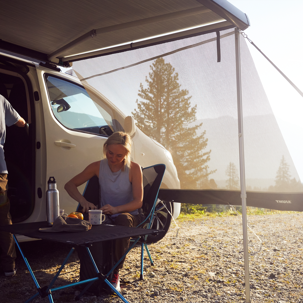 People sit under a Thule Sun Blocker Side awning side wall next to a white van.