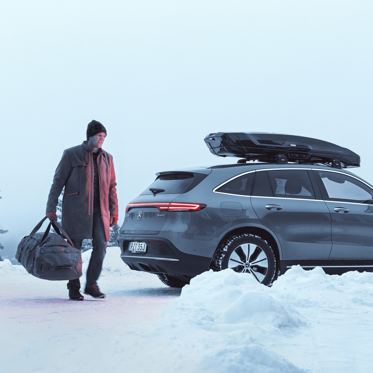 A man is unloading their ski gear from a car with a roof top box in a snowy landscape