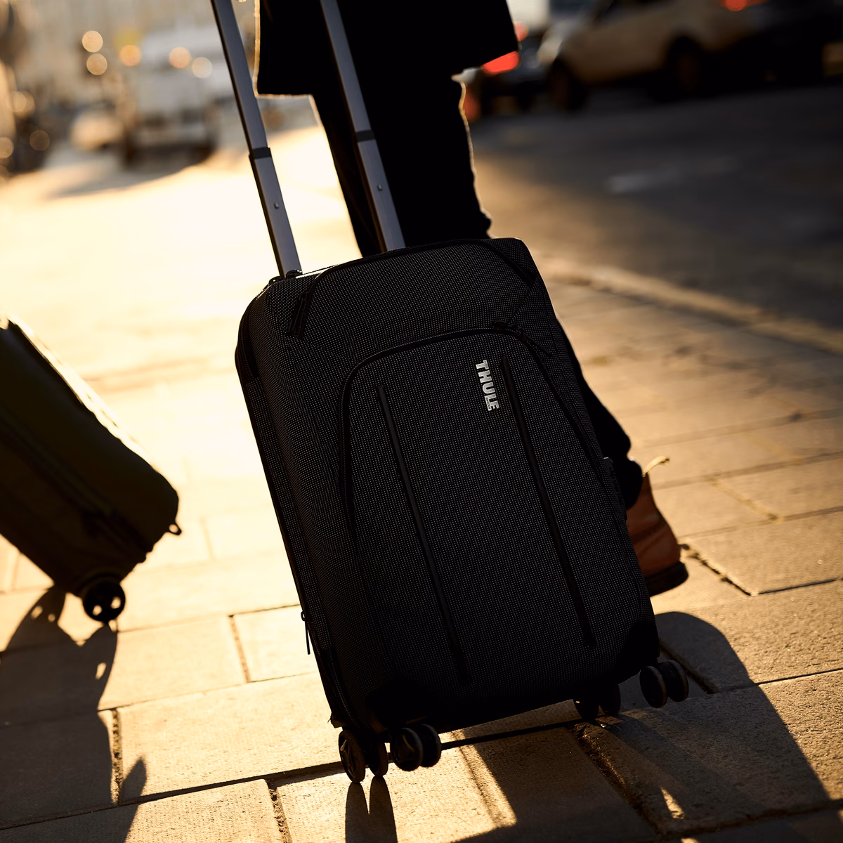 Two Thule Crossover 2 Expandable Carry-on suitcases stand on the sidewalk in the sunset.