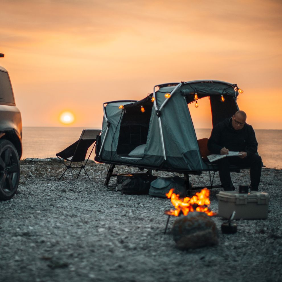 A man is sitting in his Thule Outset tent on a beach at sunset.