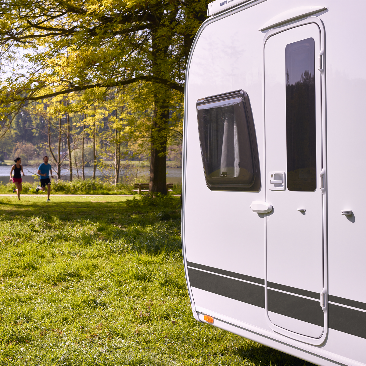 A caravan is parked in the grass and has a Thule Universal Lock caravan lock.