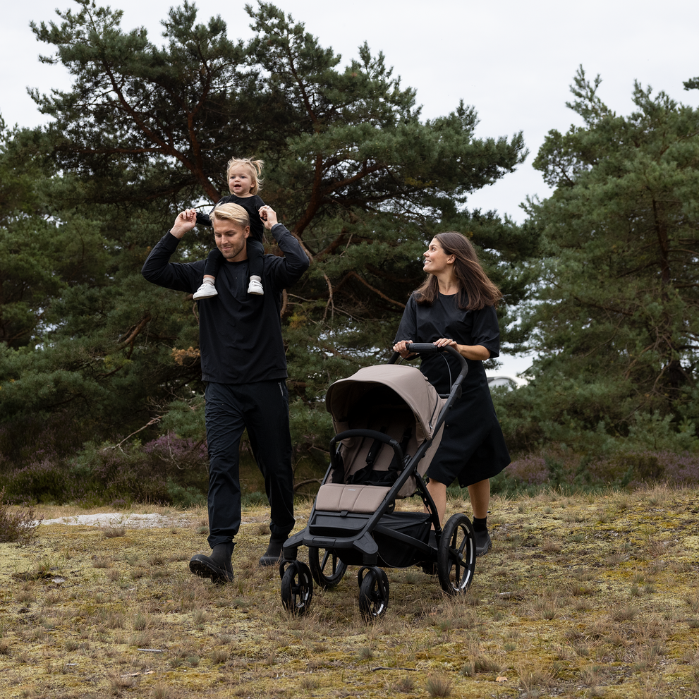 Famiglia che cammina attraverso la foresta con passeggino Thule Urban Glide a 4 ruote.
