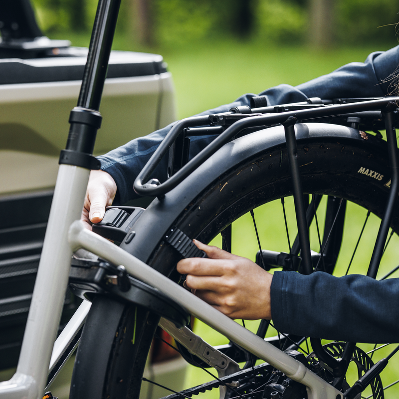 A man is securing the straps with the pump buckle of an e-bike's rear wheel mounted on the Thule Vero hitch bike rack.