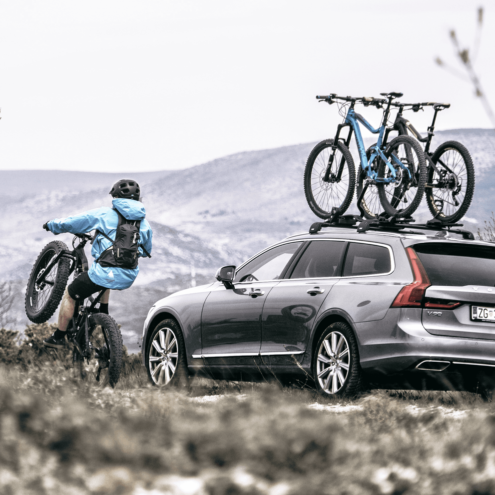 A cyclist cyles besides a vehicle with two bikes installed on the Thule ProRide roof bike rack.