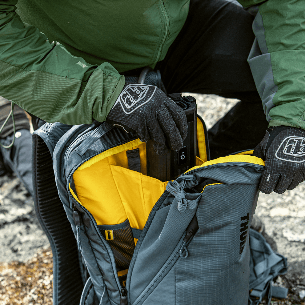 A person wearing gloves fills their blue Thule Rail 18L Hydration Backpack.