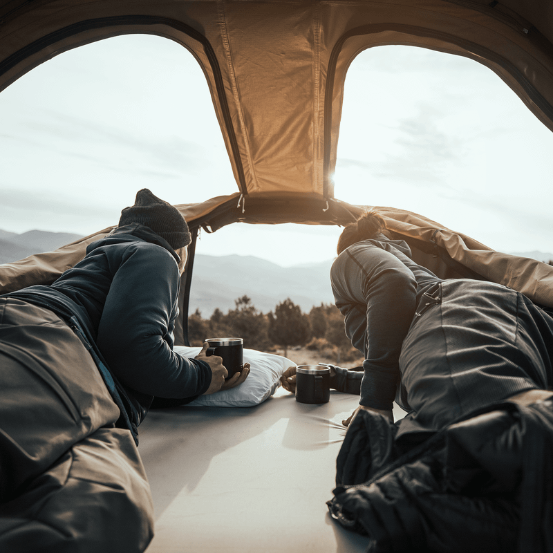 A man and a woman is looking out the skylights of a Thule Approach roof top tent