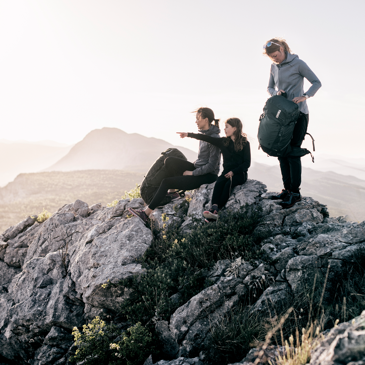 Three people sit on a rock looking out at the view, carrying Thule Versant backpacks.