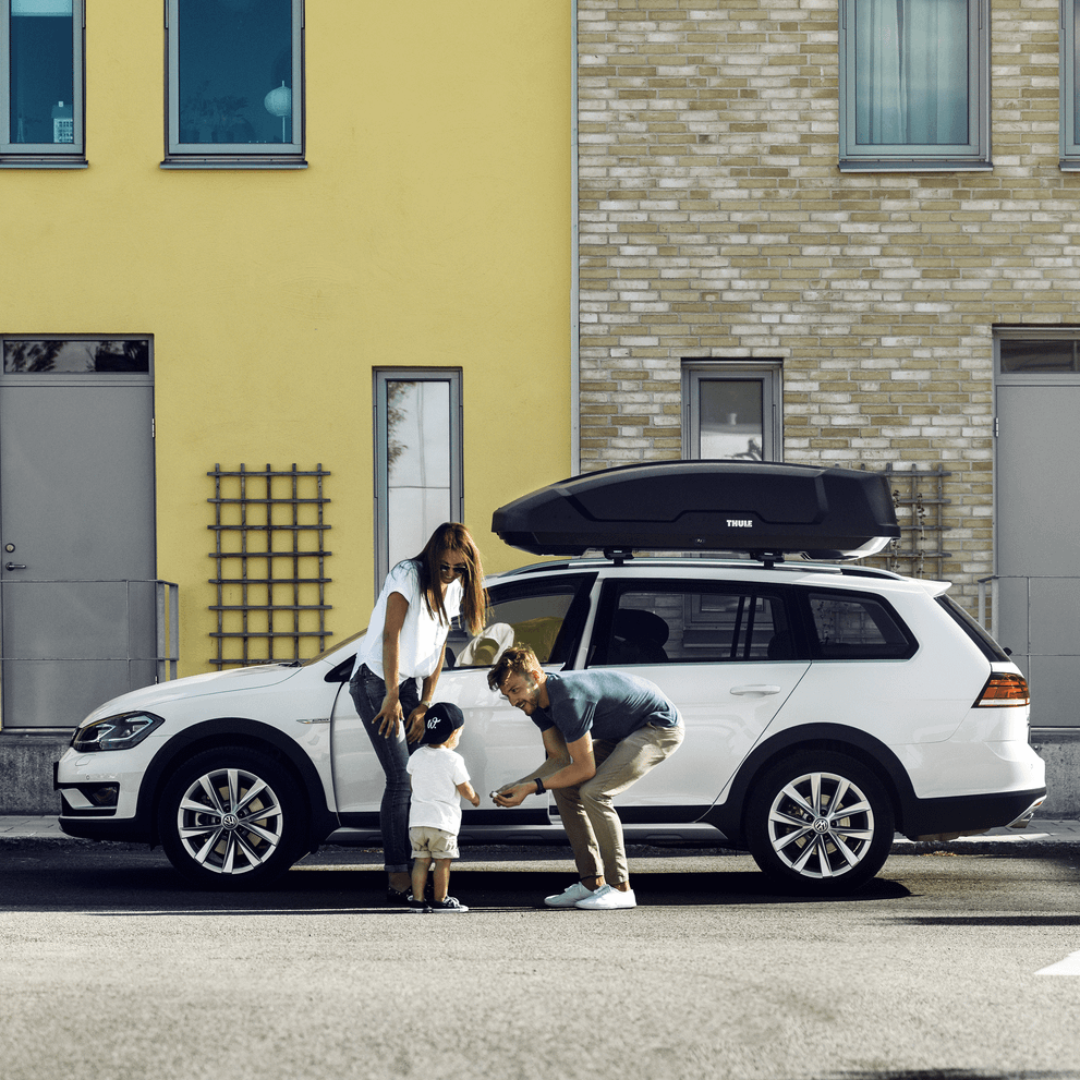 A mother and her two kids are standing in front of their car.