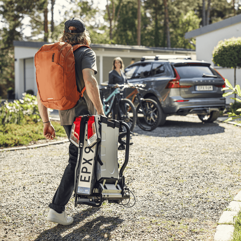 A woman is carrying a folded Thule EasyFold XT towards her car.