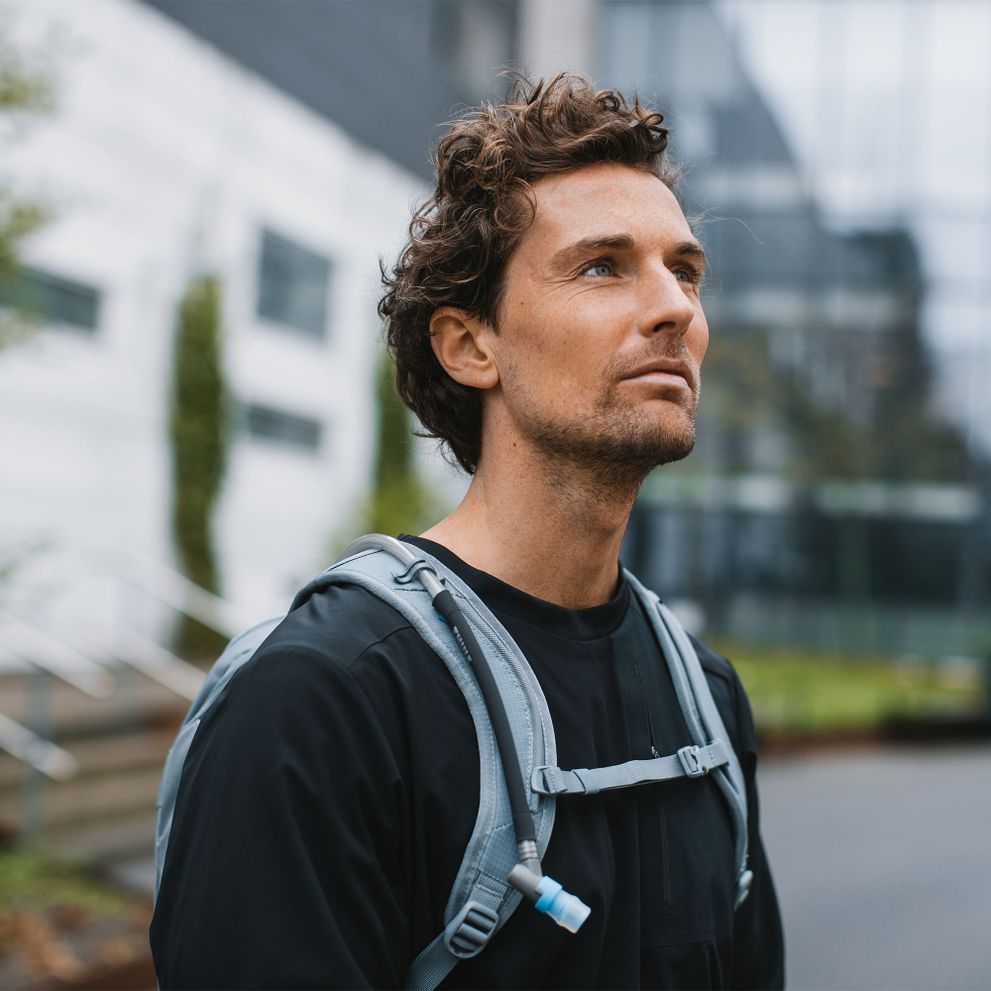 A man looks into the distance carrying a blue Thule AllTrail hydration backpack.