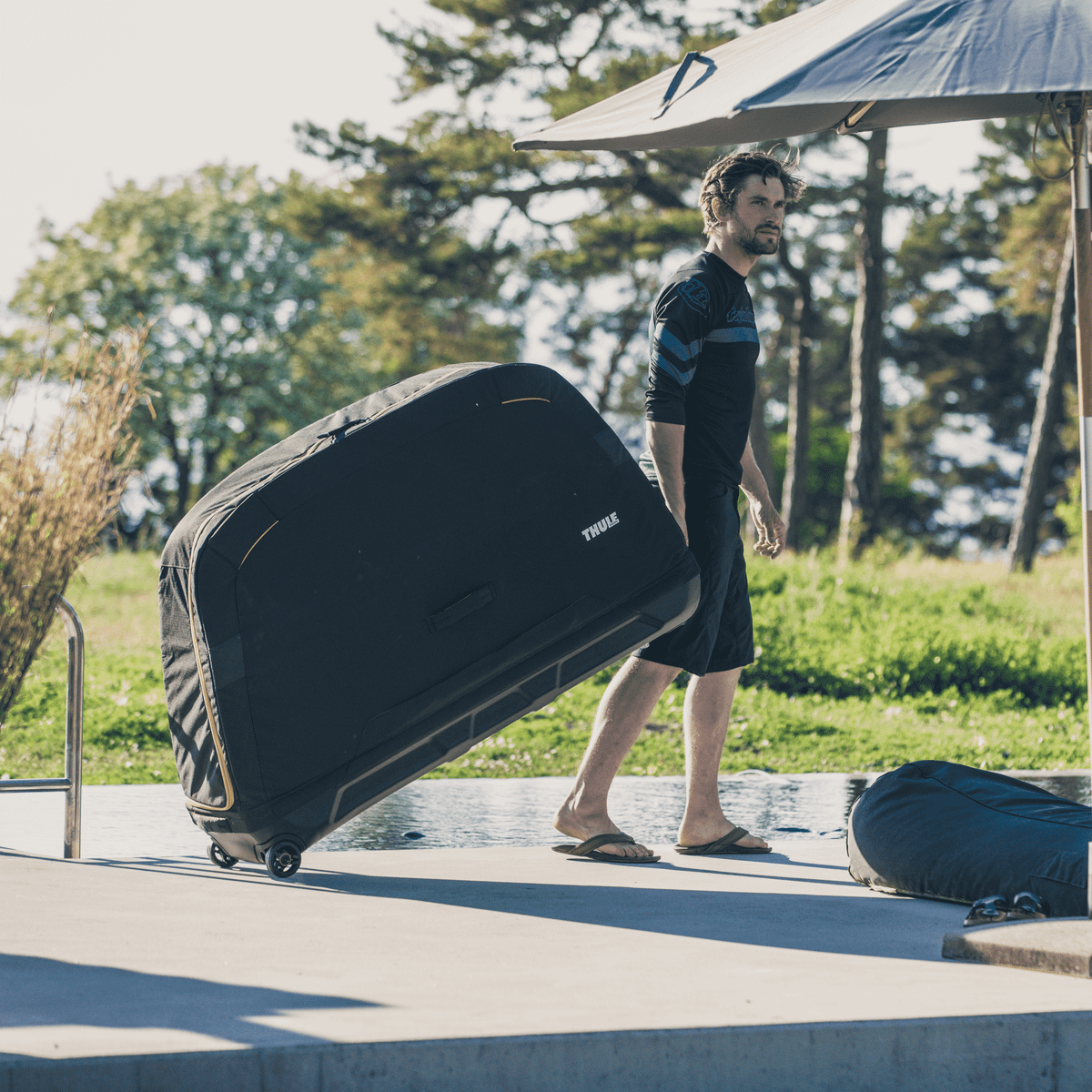 In a garden, a man pulls his black Thule Roundtrip MTB bike travel case with wheels.