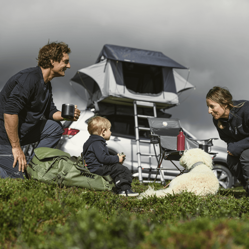 A family is sitting in the grass in front of a car with a Thule Tepui Kukenam rooftop tent