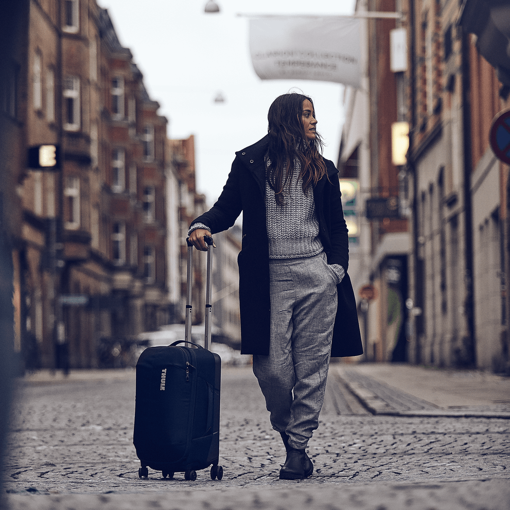 A woman stands in a city street with a Thule Subterra Carry-On Spinner suitcase.