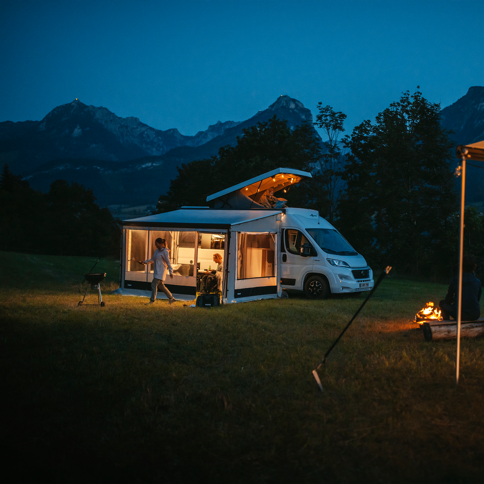 A white motorhome at night with lights and a Thule Residence G3 motorhome awning tent.