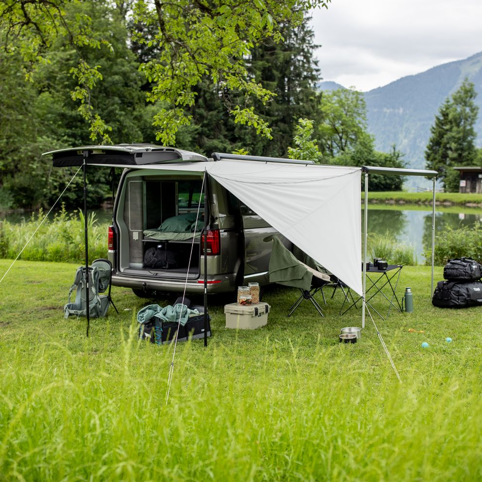 A van is parked in the mountains with a Thule Subsola panels and the trunk door open.