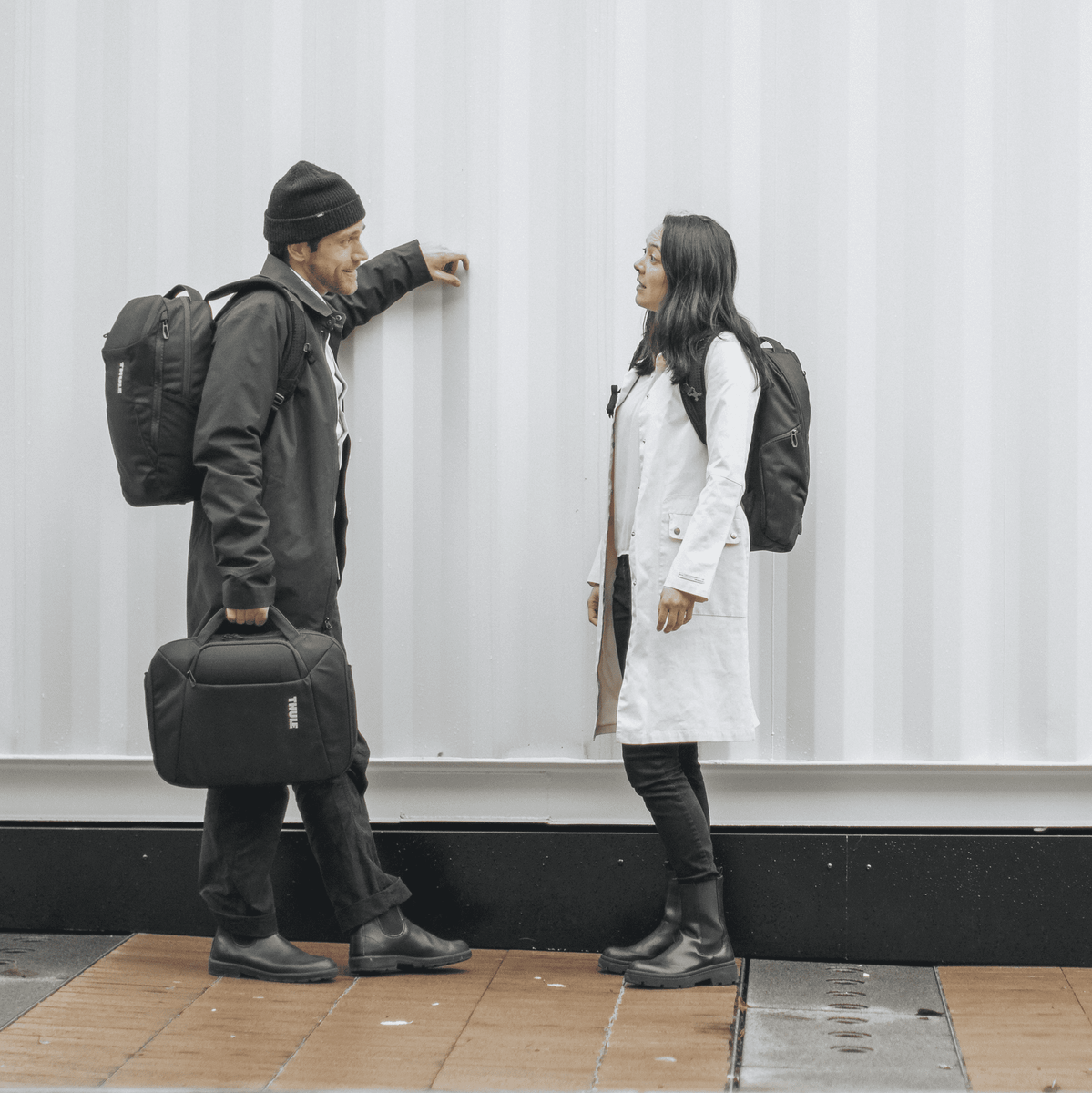 A man and woman stand by a metal structure with a black Thule Accent laptop bag.