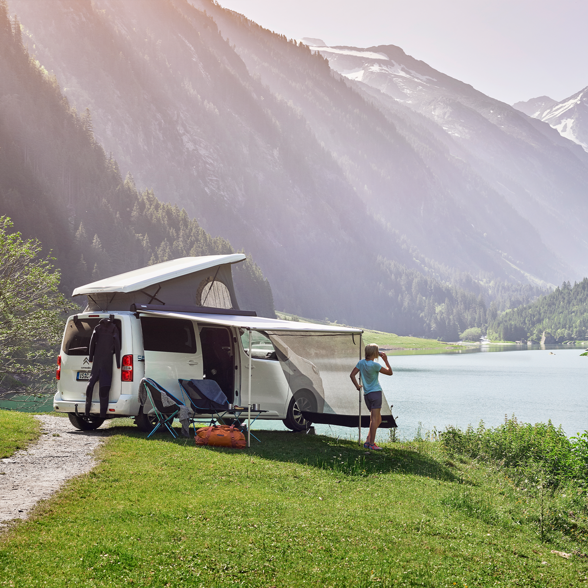 A van with a pop-up roof is parked by the lake with a Thule Sun Blocker Side awning side wall.