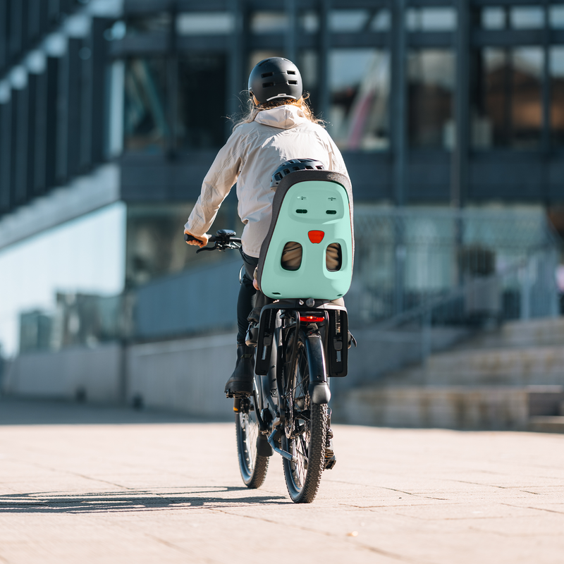 Un parent et un enfant traversent une zone urbaine moderne, avec un siège Thule Yepp Nexxt 2 bien visible.