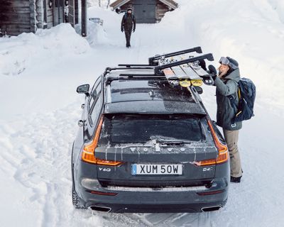 Una mujer se encuentra de pie en la nieve mientras descarga sus esquís de un vehículo con un portaesquís.