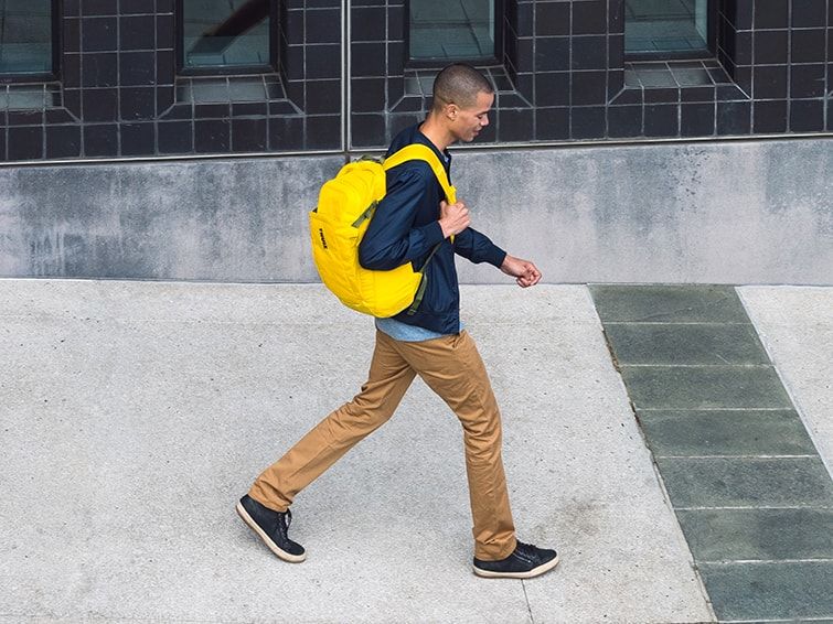 A man walks down an urban street carrying a yellow laptop backpack for men.