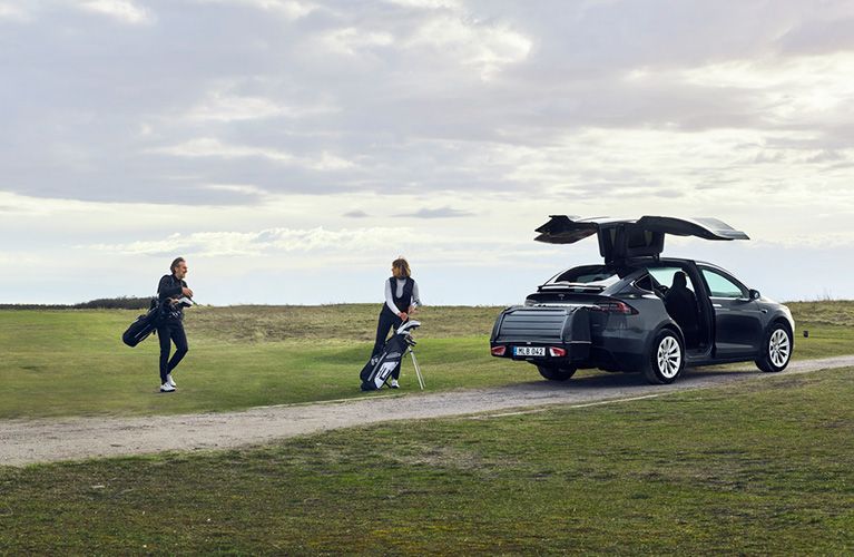 カップルが、EV車に装着したリアカーゴキャリアにゴルフクラブを積み込んでいます。