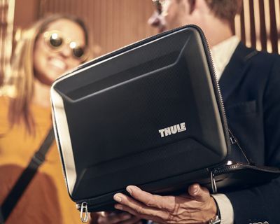 Two people stand talking holding a laptop case.