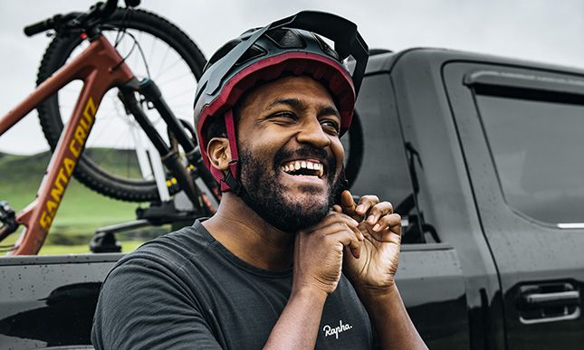 Eliot Jackson befestigt seinen Helm, im Hintergrund ein Pick-up und ein Thule Pick-up-Fahrradträger mit einem Fahrrad.