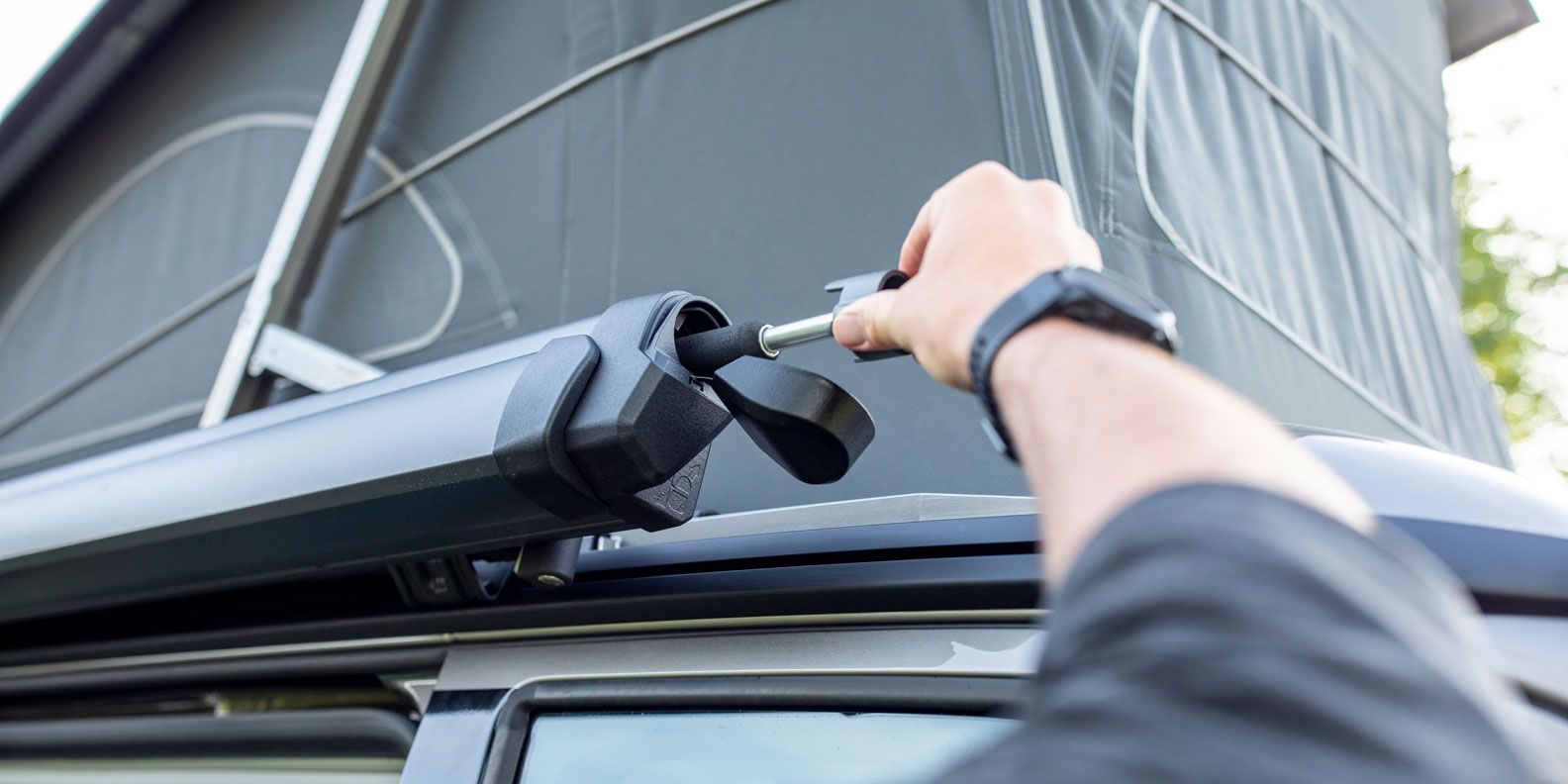 A person inserts their hand crank into the Thule Sidehill compact van awning.