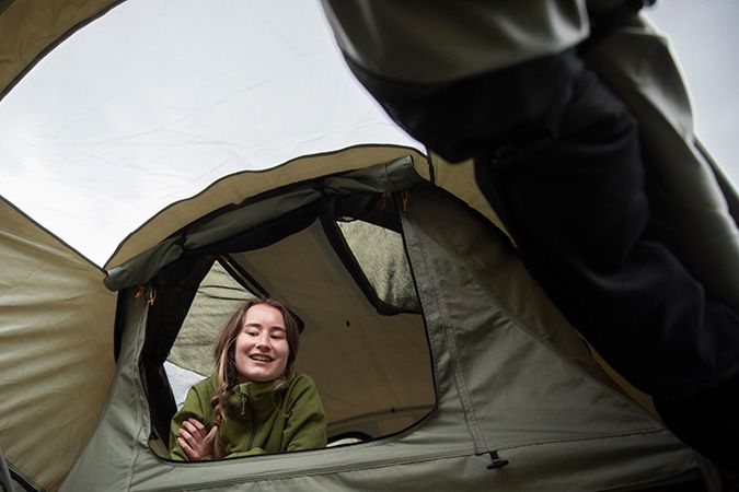 A woman sits in a Thule Approach rooftop tent looking down at a man. 