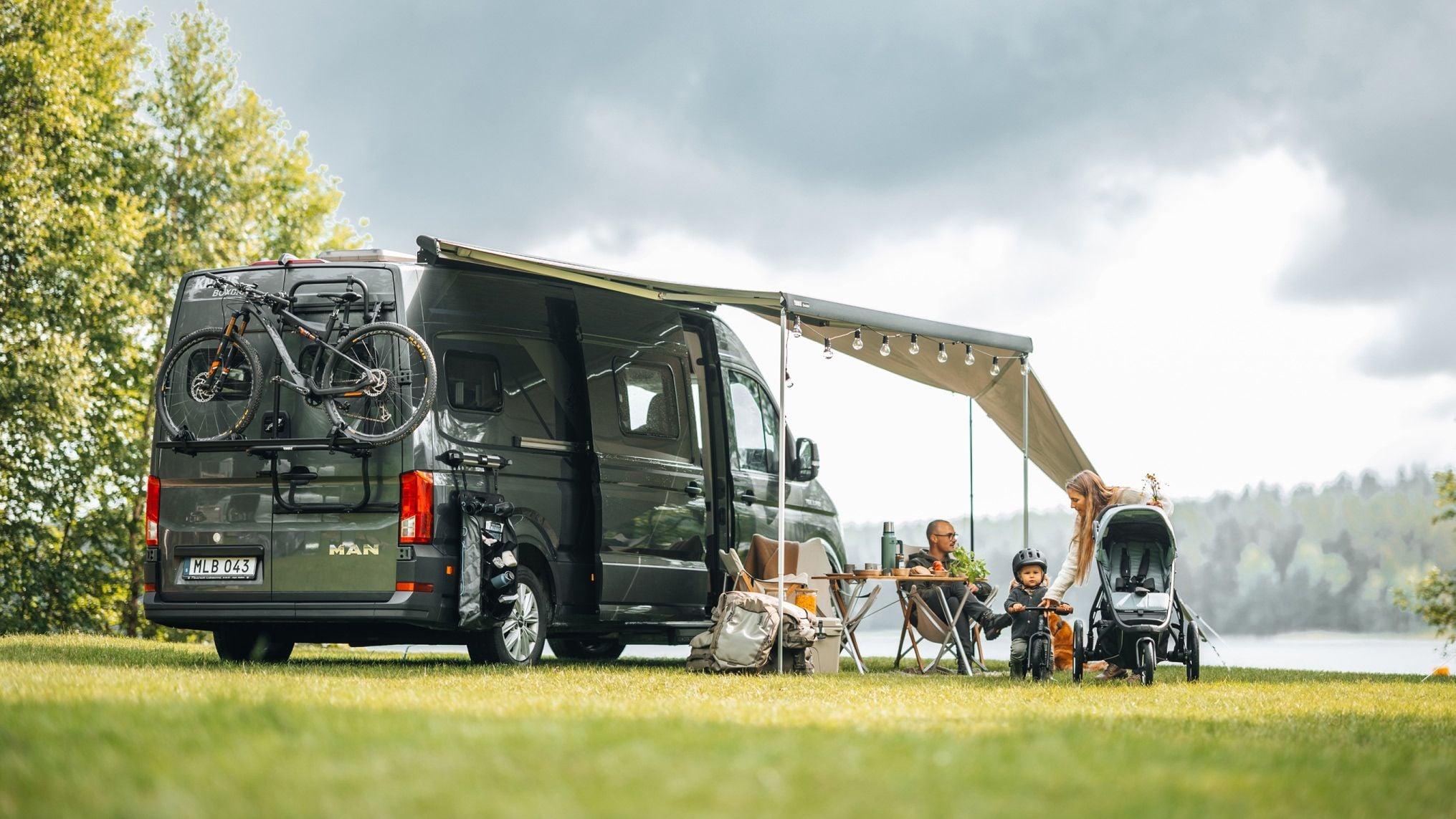 Van camping-car avec panneaux d’auvent Thule Subsola installés à côté d’un terrain de camping au bord du lac.